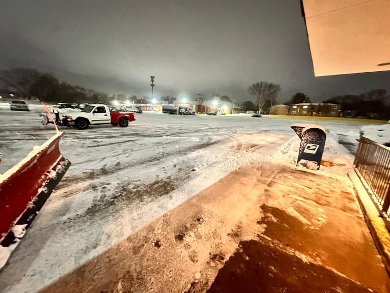 Plow blade at a lot entrance at night with a second truck working behind.